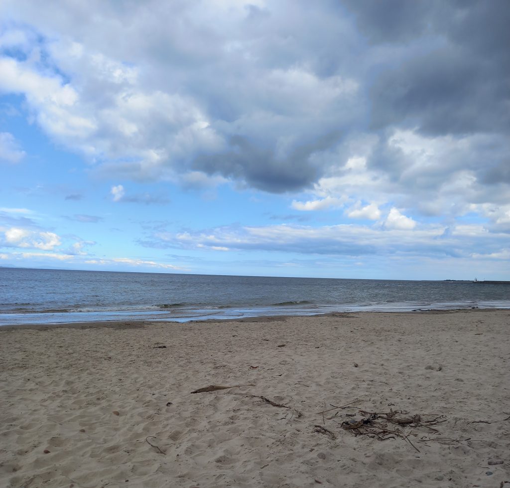 A picture of Nairn beach near Inverness, with a wide sandy shore alongs the ocean waves, with a mostly cloudy sky overhead.