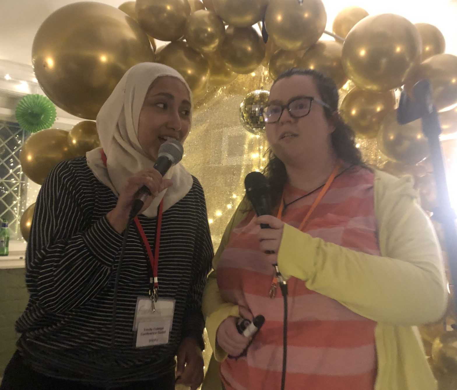 A picture of me and a friend singing karaoke in front of a balloon arch.