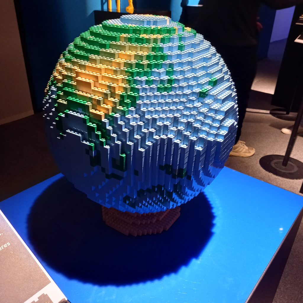 A circular blue and green globe of Earth, made out of lego, standing on a base